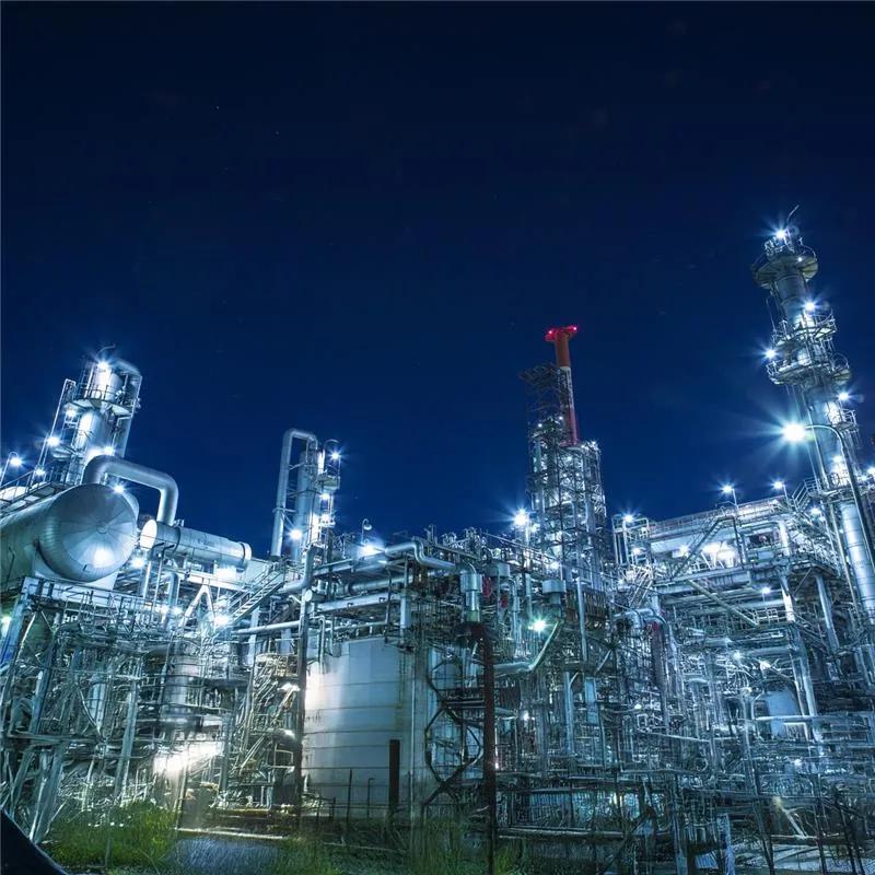 View of a lit up petrochemical refinery plant at night. 