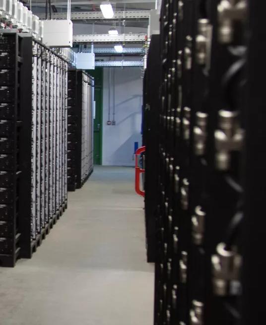 A side view of several rows of dark gray or black server hardware racks, showing the cable management and hardware depth within the server frames.