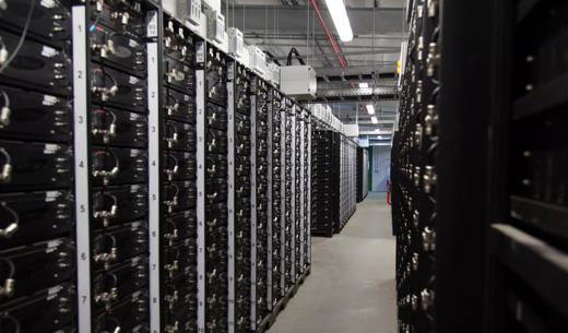 A corridor lined with rows of black server racks, illuminated by overhead lights.