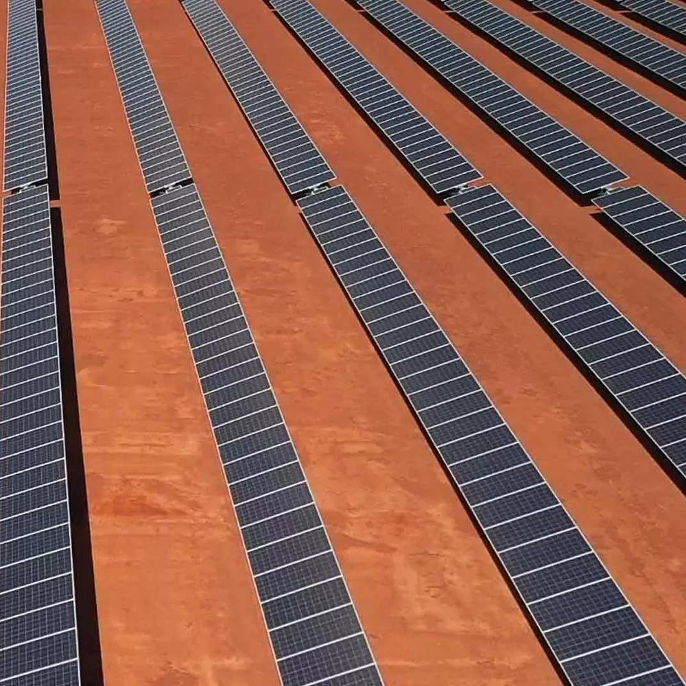 Aerial view of two workers walking passed solar panels across a large solar farm.