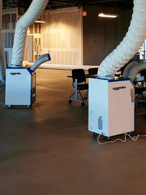 Portable Aggreko cooling unit connected to flexible air ducts indoors.