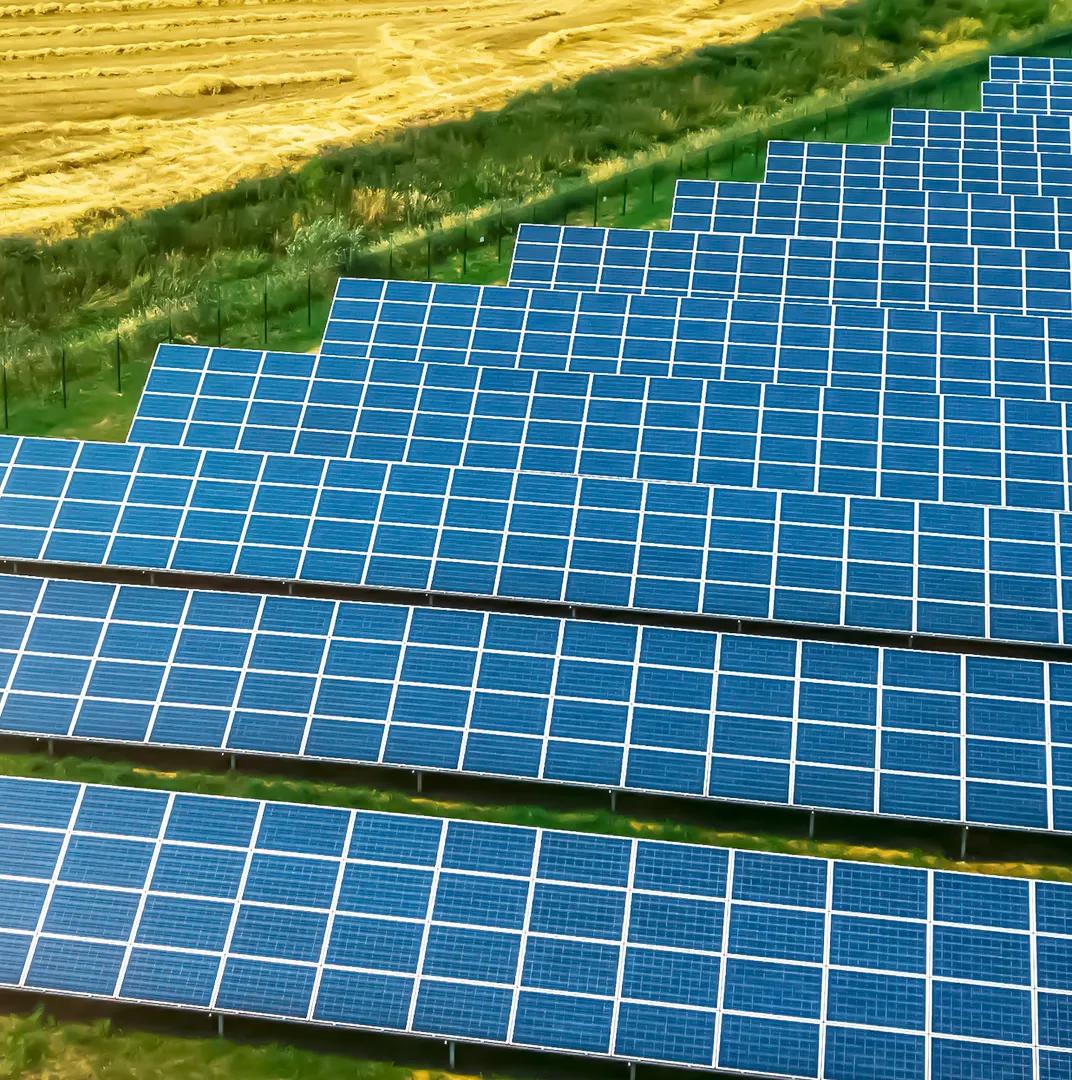 Aerial view of a large row of solar panels in a grassy field.