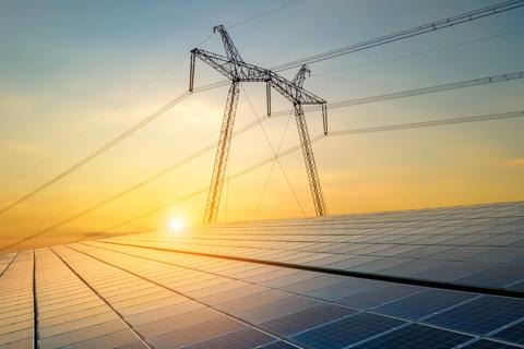Ground shot of solar panels with a transmission tower in the background during a tell sunset.  