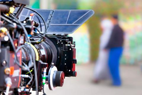 A professional broadcasting camera pointing towards a pair of blurred-out people.