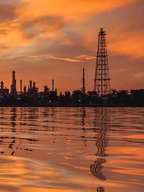 Industrial facility silhouetted against a sunset over the water.