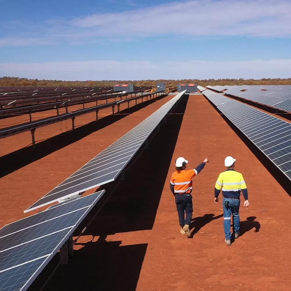 Two workers walking between two rows of solar panels in a red field