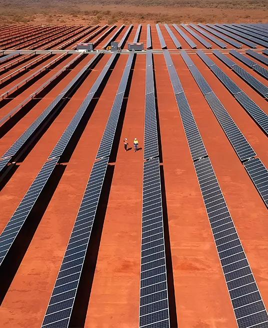 Aerial view of a large solar farm featuring rows of solar panels set on red desert terrain.
