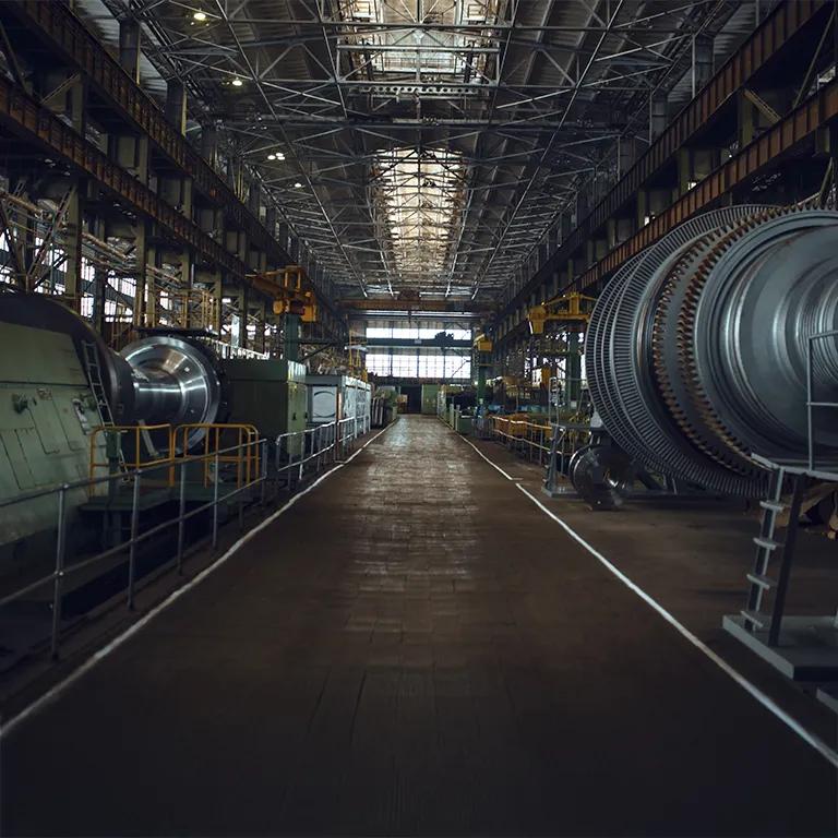 A long-exposure, wide-angle view down the central aisle of a large, high-ceilinged industrial power plant or factory, showing large turbine generators and machinery on both sides.