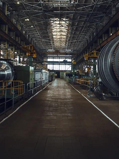A long-exposure, wide-angle view down the central aisle of a large, high-ceilinged industrial power plant or factory, showing large turbine generators and machinery on both sides.