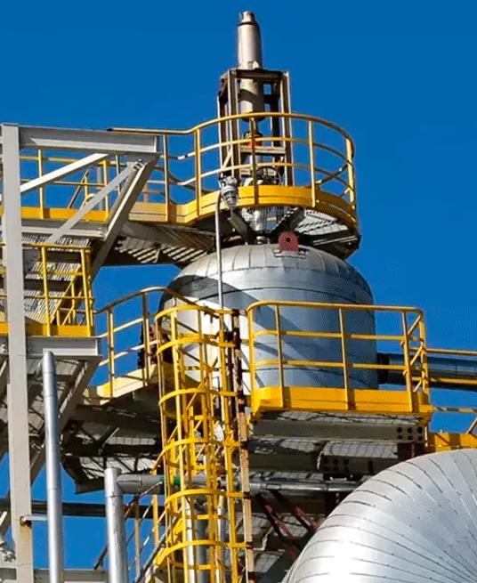 View of the top of a refinery tower against a blue sky.