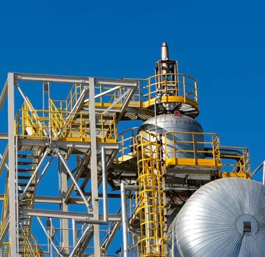 Metal pipes and an industrial framework with a yellow staircase against a clear blue sky.