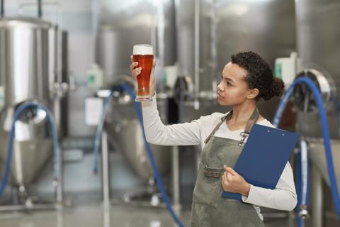 Waist up portrait of young African-American woman holding beer glass while inspecting quality of production at brewing factory, copy space