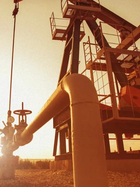 Un travailleur à côté d’une plateforme pétrolière dans un champ au coucher du soleil.