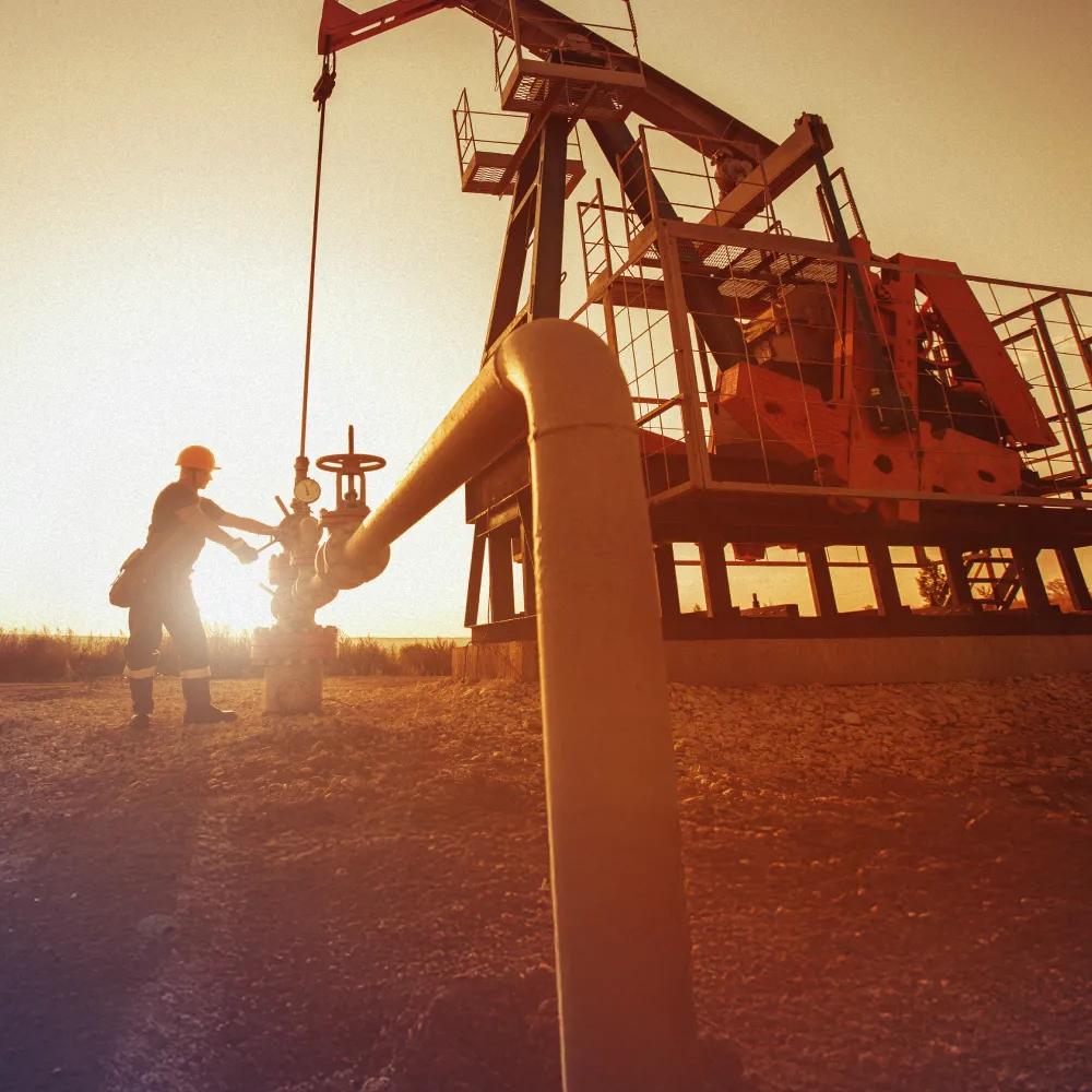 A worker next to an oil rig on a field against a sunset