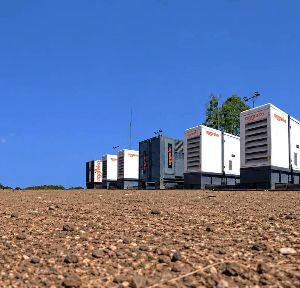 A line of large industrial Aggreko generators against a blue sky and a flat, barren landscape.