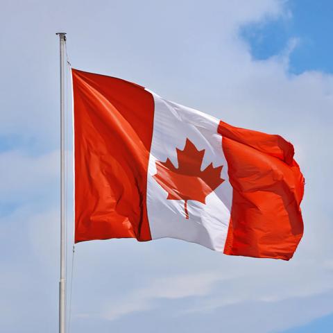 Canadian flag waving in the wind against a blue sky with light clouds