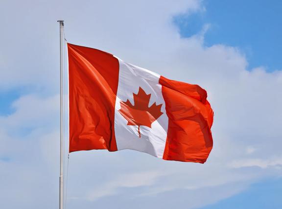 Canadian flag waving in the wind against a blue sky with light clouds