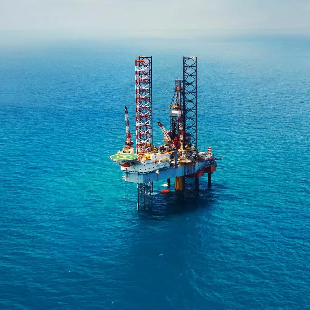 Offshore oil drilling platform with cranes, equipment, and support vessels in blue water.