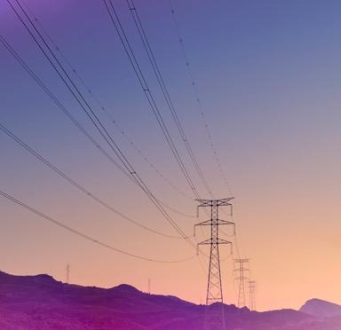 Power lines stretch across a gradient sky at sunset over silhouetted mountains.