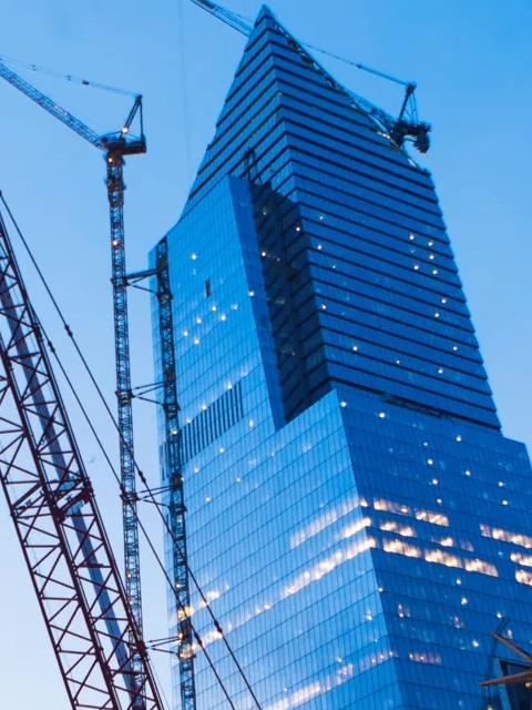 Low-angle shot of multiple cranes in a skyline filled with buildings.