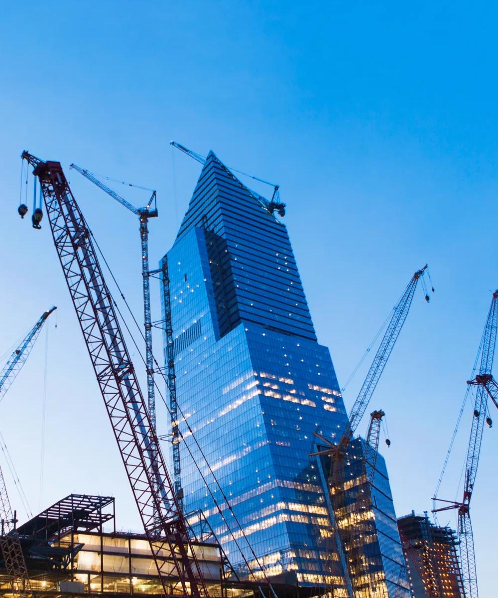 Low-angle shot of multiple cranes in a skyline filled with buildings.