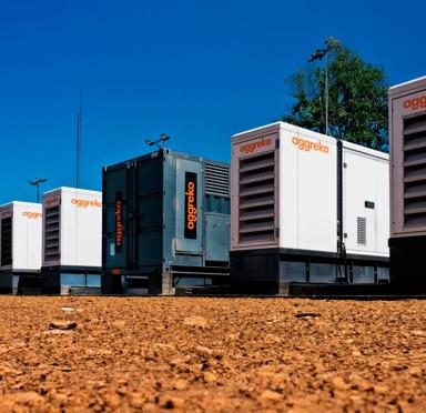 A row of Aggreko generator units on a gravel surface under a clear blue sky.