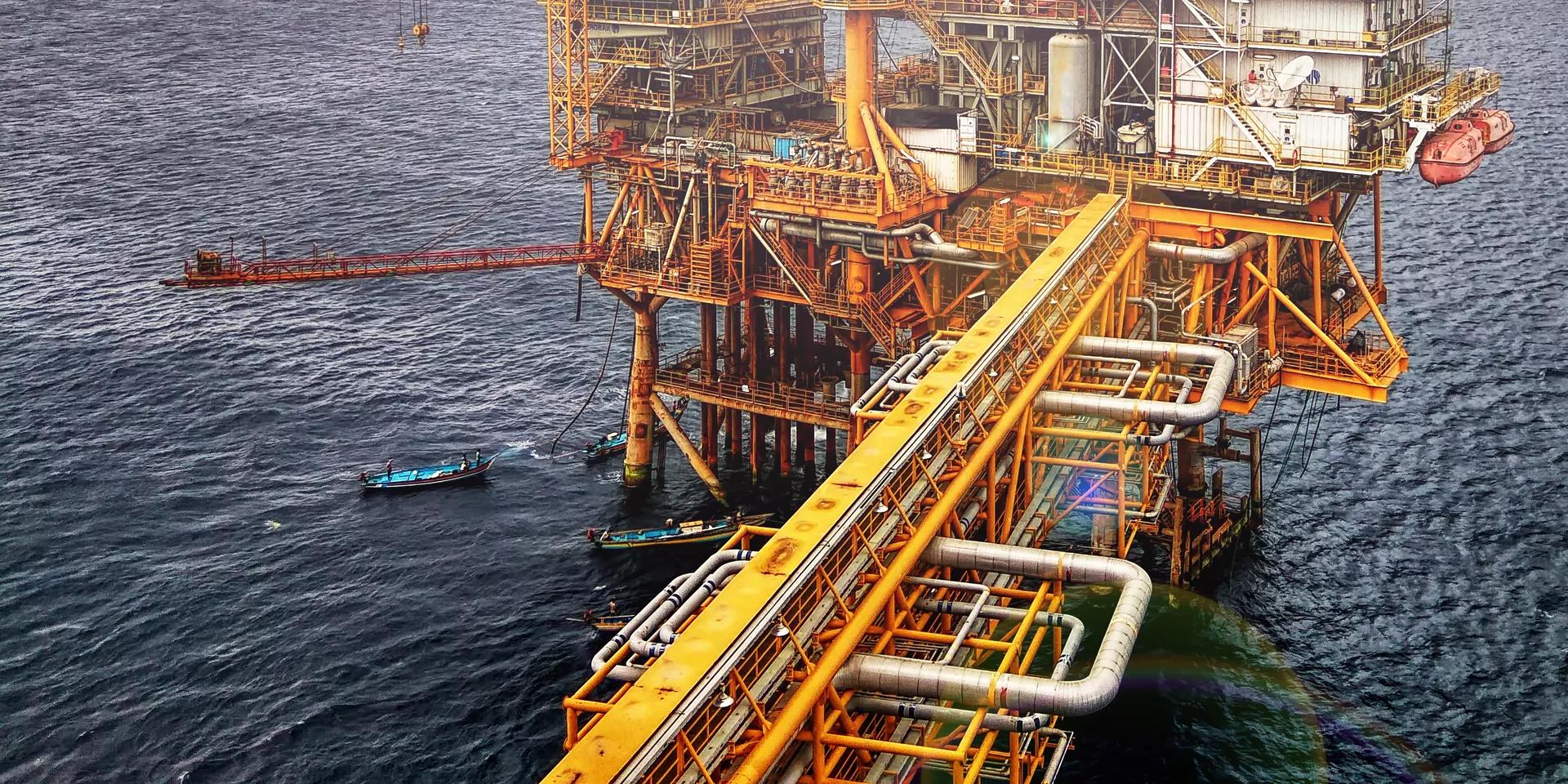 A distant oil rig in the sea under a blue, somewhat cloudy sky