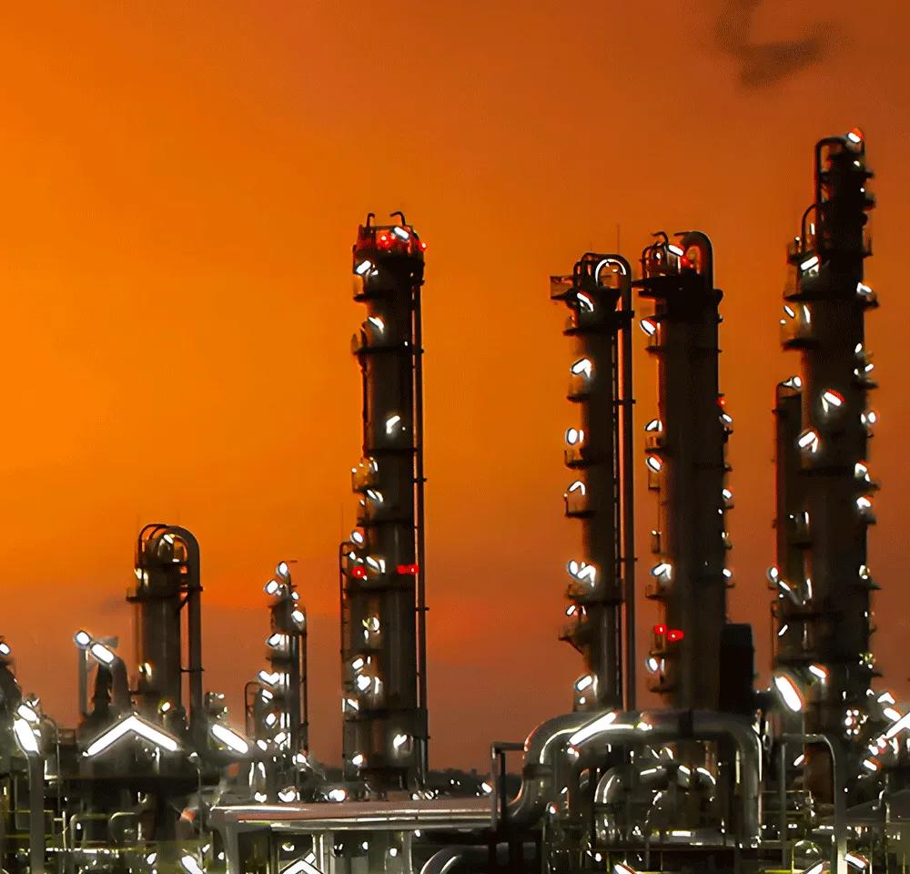 Aerial view of a lit-up refinery at night during an orange sunset.