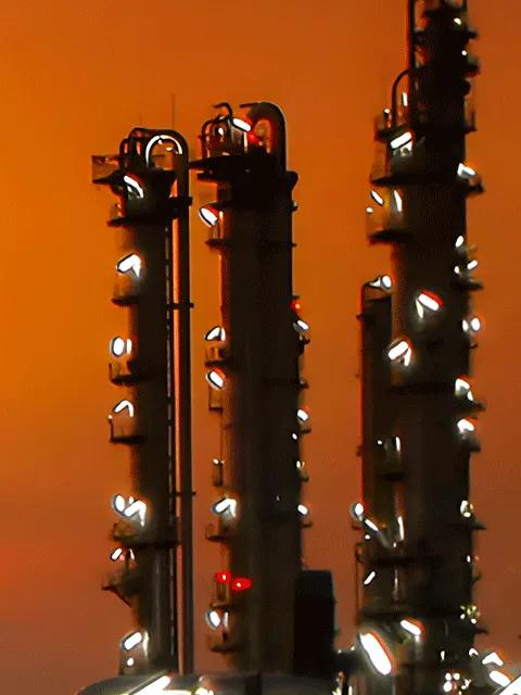 Aerial view of a lit-up refinery at night during an orange sunset.