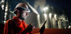 Caucasian man engineer using digital tablet working late night shift at petroleum oil refinery in industrial estate