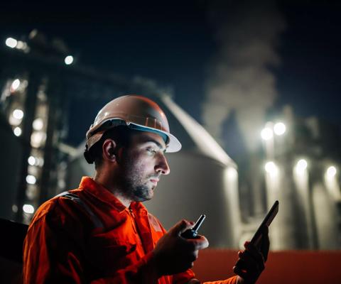 Caucasian man engineer using digital tablet working late night shift at petroleum oil refinery in industrial estate