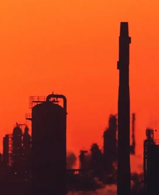 View of refinery towers silhouette against a red sky.
