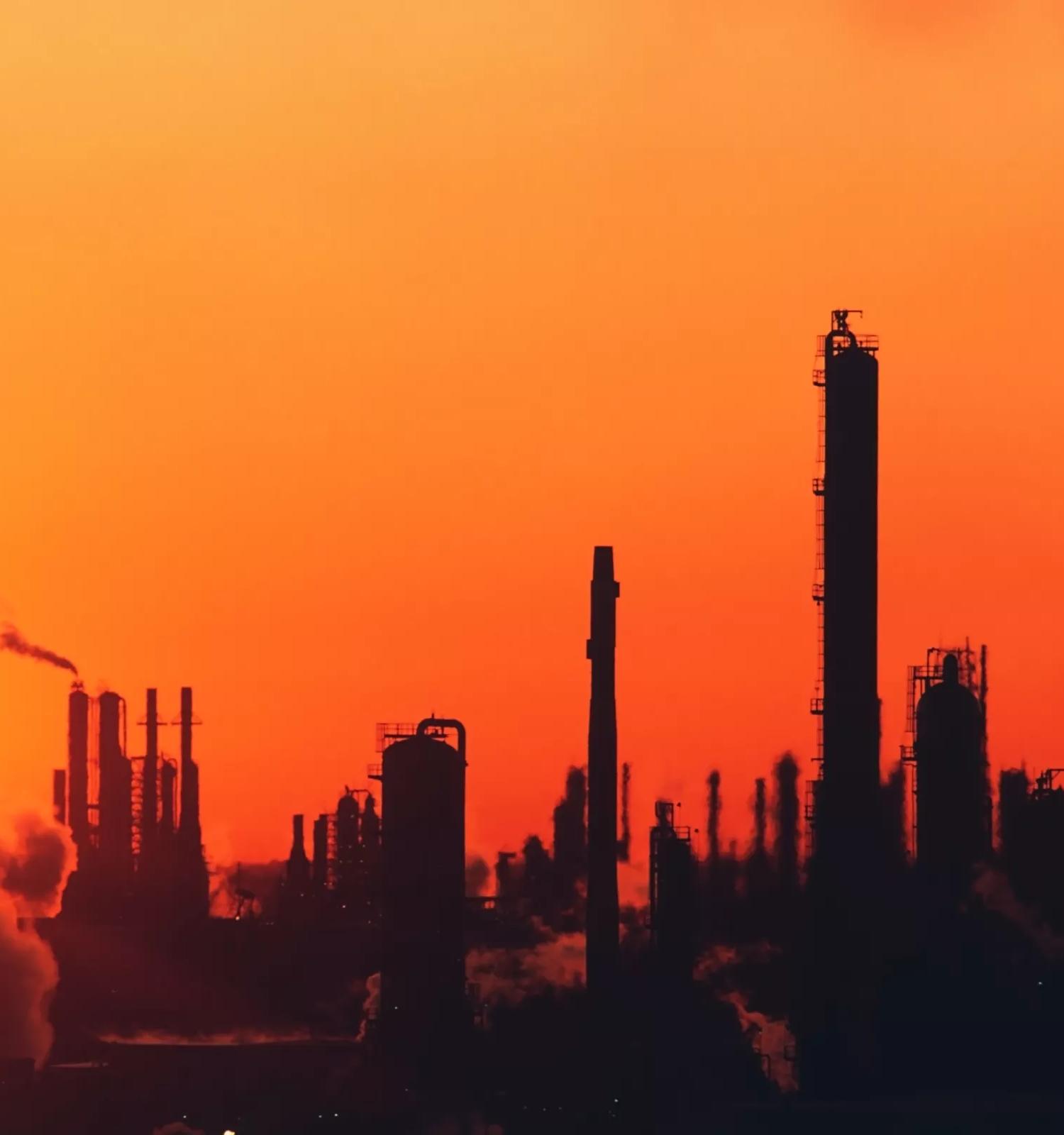 View of refinery towers silhouette against a red sky.