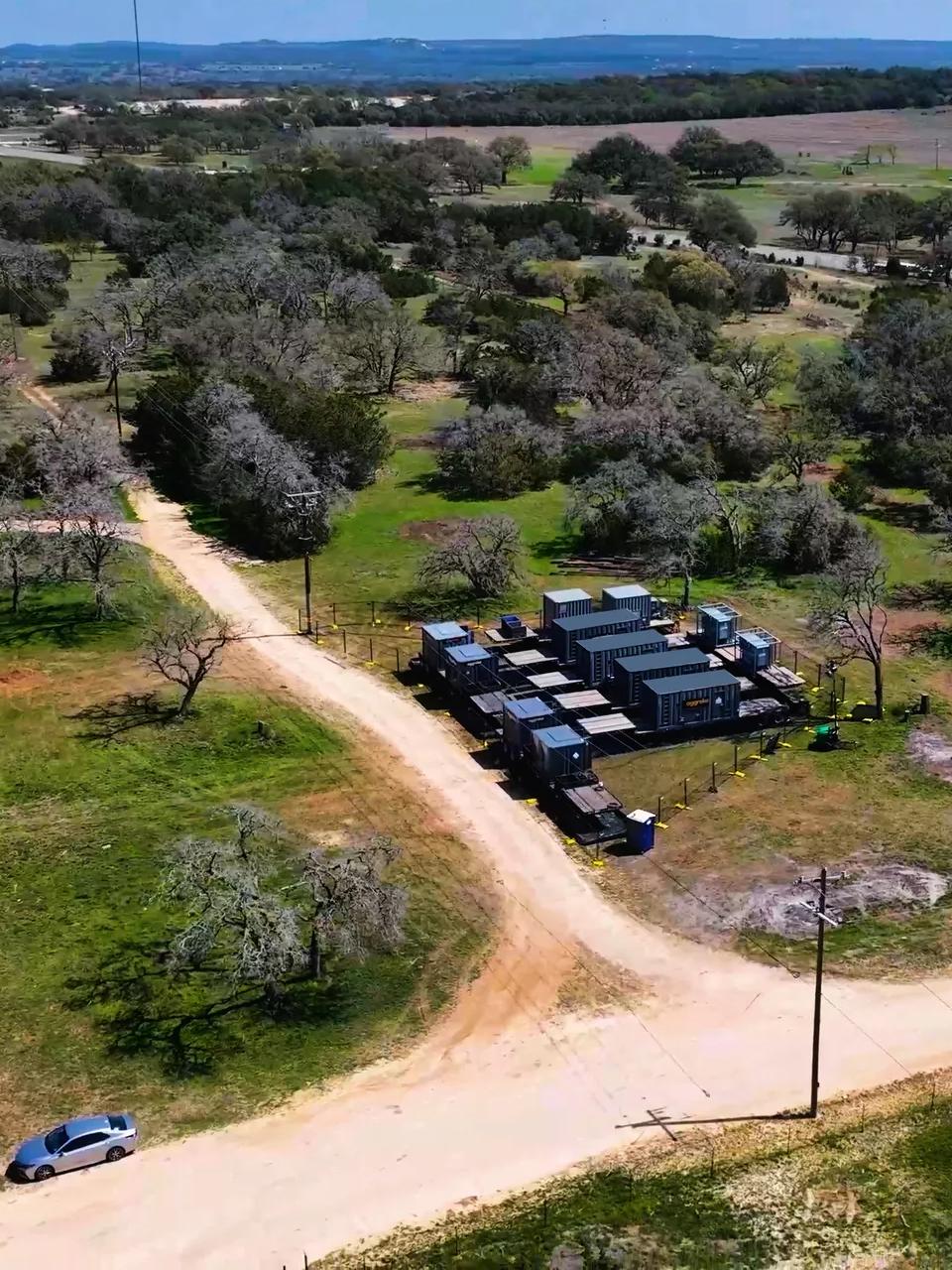 Black rectangular equipment in the middle of a green field and next to a dirt road