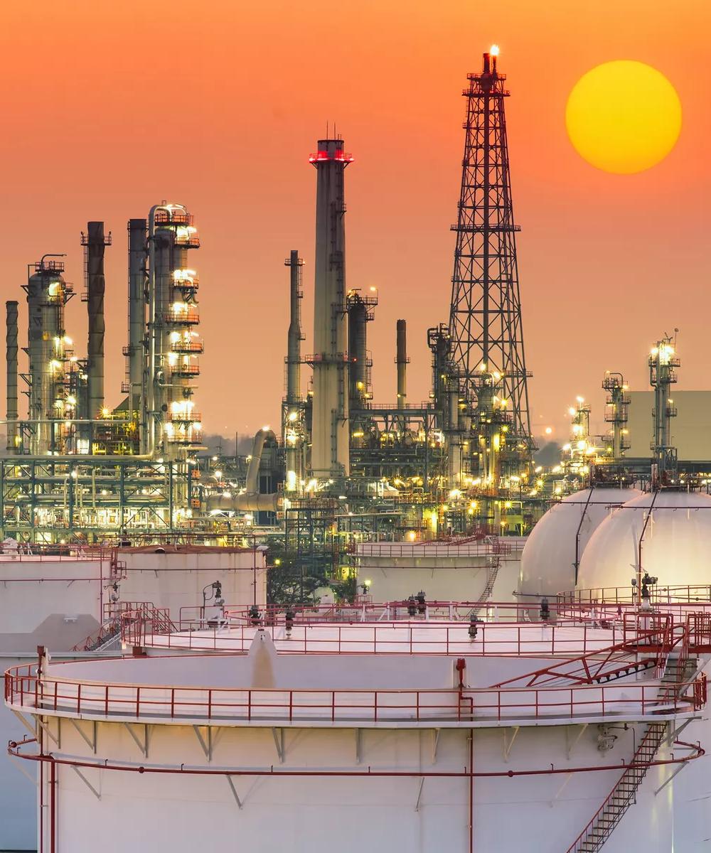 View of a lit-up refinery against an orange sky.