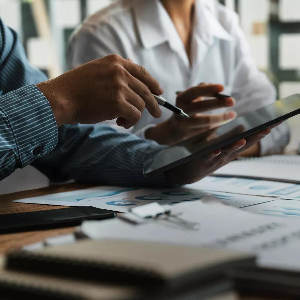a person holding a tablet with another person in a desk with papers and notebooks