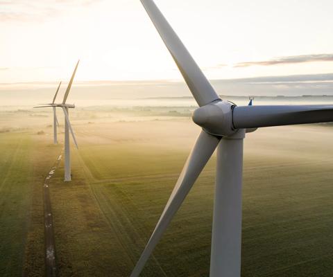 Aerial view of three wind turbines in the early morning fog at sunrise in the English countryside